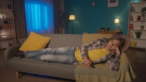 Tired Man Lies on the Couch Late at Night and Watches TV The Man Cannot Find Anything Interesting
