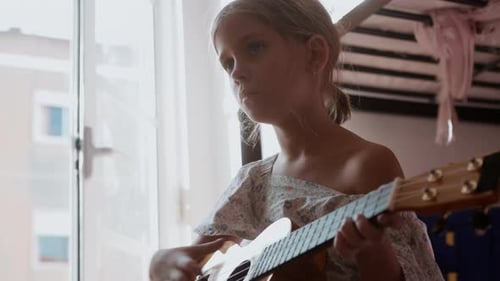 Young Girl Concentrating While Playing Ukulele Indoors