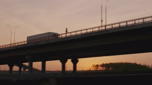 White semi truck with cargo trailer driving on road bridge, transportation of goods at sunset