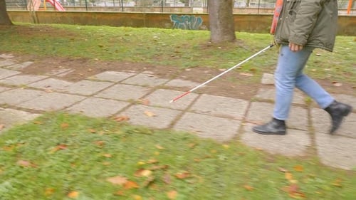 junge blinde Frau geht mit ihrem Stock auf dem Bürgersteig im Park