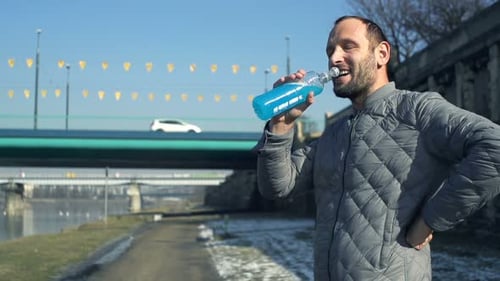 Male Jogger Drinking Isotonic Drink Near River in City, Super