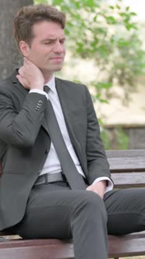 Man in Suit Sitting on Bench with Neck Pain