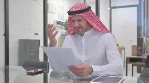 Frustrated Man Reviews Documents in Modern Office