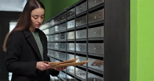 Woman is Opening Her Mailbox Inside a Cluster of Mailboxes for Her Apartment Payment Notification