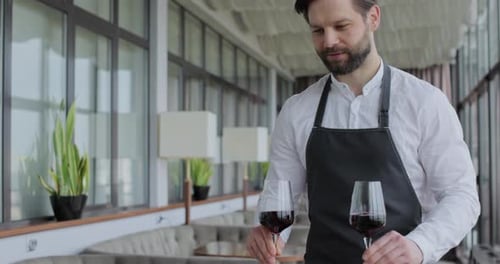 Waiter Carries Two Glasses of Wine to a Young Couple at a Table in a Restaurant