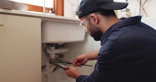 Plumber repairing sink pipes with large wrench