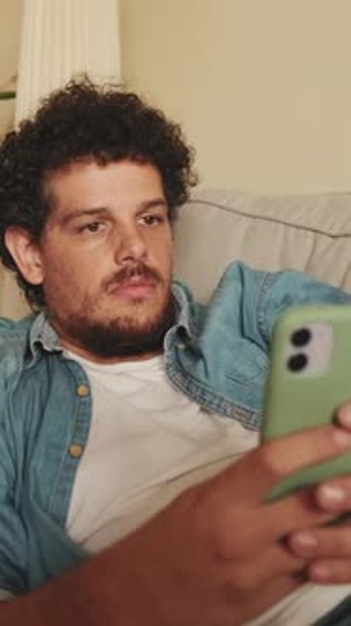 Young Adult Using Smartphone Lying on Sofa