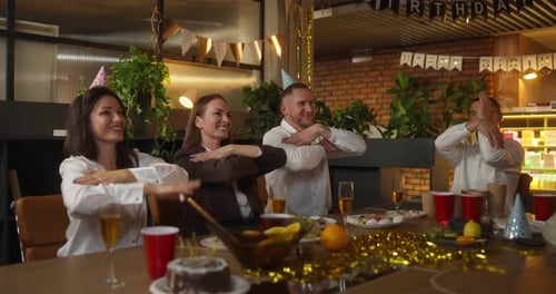 Four Office Workers in Business Suits Sit at a Festive Table and Dance During a Fun Corporate Party