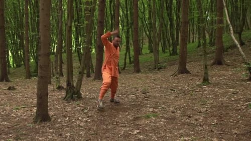 Man In Orange Uniform Practicing Kung Fu Moves In The Woods. - wide shot