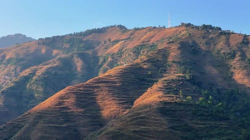 aerial shot of rolling green hills covered in dense forests under a vibrant blue sky