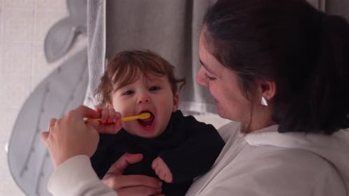 Woman Brushing Baby's Teeth in the Bathroom