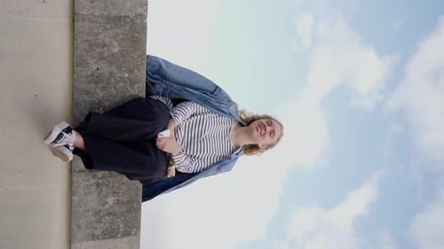 Vídeo em câmera lenta de uma jovem mulher com uma jaqueta jeans sentada perto do Louvre, em Paris, vista vertical