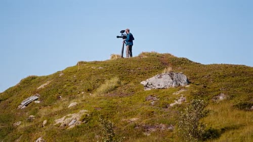 Filmmaker with Camera on Grassy Hillside