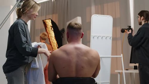Assistant Putting Bathrobe on Male Bodybuilder during Studio Photoshoot