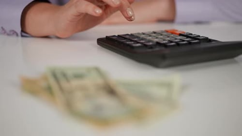 Mãos femininas de closeup contam com uma calculadora que fica sobre uma mesa branca, as notas de papel estão fora de