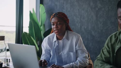 At a Cafe a Male and Female Black Business Duo Sit Beside a Laptop Exchanging Ideas and Using Hand