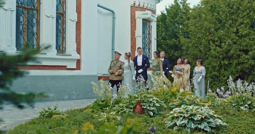 People in Historical Costumes Walk in Pairs Near a Beautiful Mansion