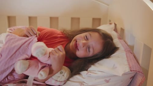 Smiling Girl Lying in Bed Hugging Stuffed Animal