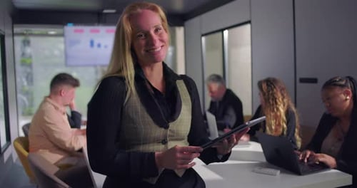 Cheerful female executive holding tablet while standing at head of conference table during office