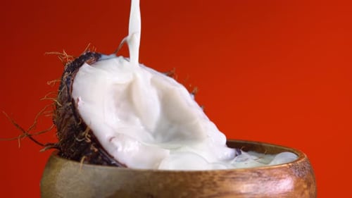 Coconut milk pouring, dripping coconut water, drops of coconuts oil over red background.