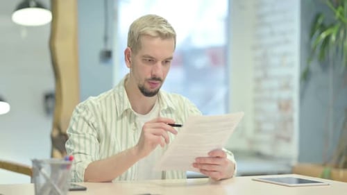Young Man Reading Documents, Paperwork in Office