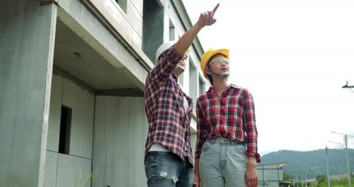 Junger asiatischer Mann und Frau zeigen mit der Hand, Sicherheitsausrüstung für Wirtschaftsingenieure auf der Baustelle.