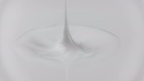 Goutte de lait frais qui tombe et éclabousse dans une mare laiteuse depuis le haut (anneaux au ralenti et sommet ondulé)