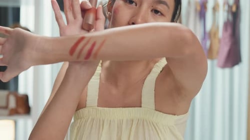 Asia lady vlogger looking at camera recording swatch apply new collection lipstick on arm show.