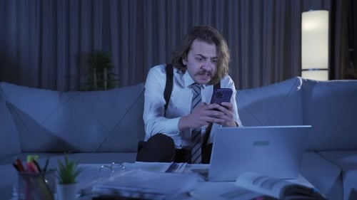 Frustrated Man Uses Smartphone at Home at Night