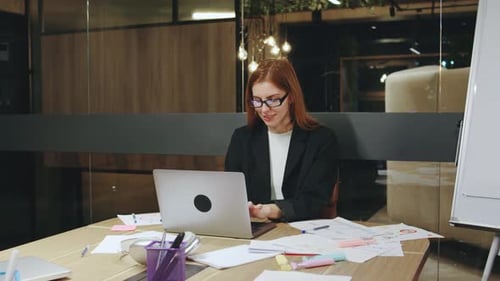 In a Modern Workspace a Dedicated Businesswoman Works Late Analyzing Documents on Her Laptop