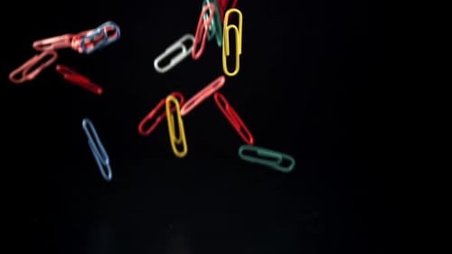 Multicolored Paper Clips Fall on a Black Background Filmed on a Highspeed Camera at 1000 Fps