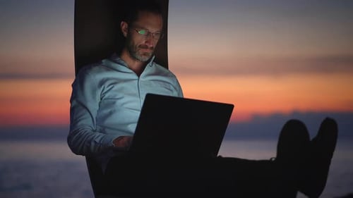 Man Works on Laptop at Sunset Over Water