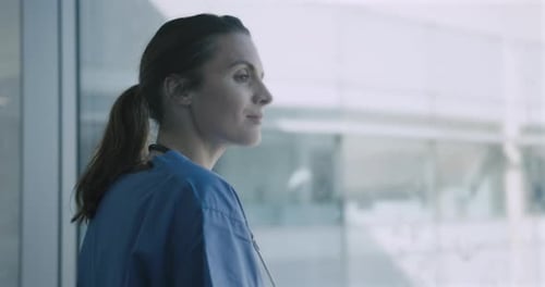 Krankenschwester im medizinischen Gestrüpp schaut nachdenklich aus dem Fenster