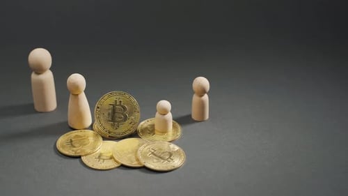 Close-up of gold bitcoin coins and wooden figures on a grey background