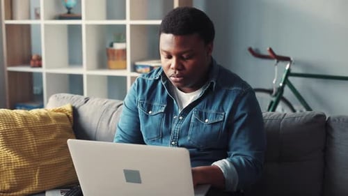 Focused man using laptop on sofa indoors