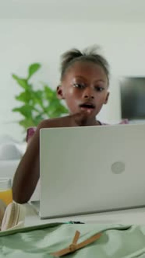Vertical video: Leaning girl wearing purple top studying at home table, monitoring laptop, thinking
