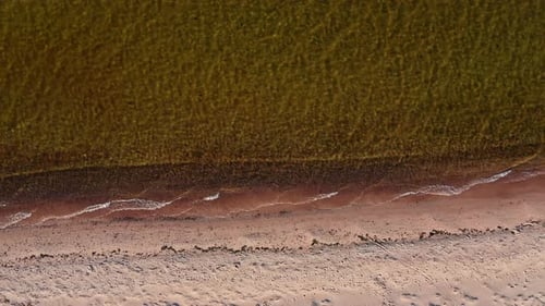 Flug über die Küste mit Wellen, die langsam am Strand hereinrollen