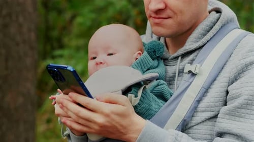 Father and Newborn Baby in a Sling in the Autumn Forest Man with Mobile Phone Happy Family