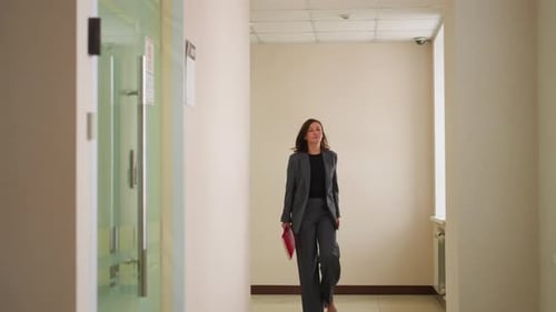 Businesswoman Walking Down Office Hallway Holding Red Folder