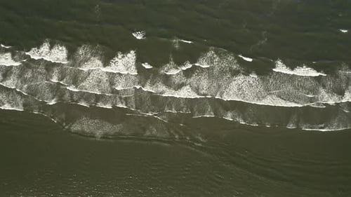 Vista de pájaro de playa volando sobre capas de pequeñas olas oceánicas rompiéndose