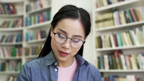 Asian female student studies by reading books, taking notes at the university library. Young woman