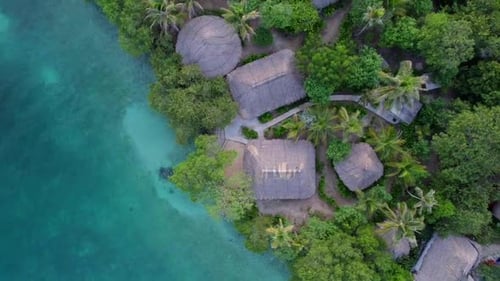 Exotic thatched-roof bungalows on turquoise crystal water in Caribbean island. Aerial orbit