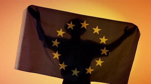Silhouette Holding European Union Flag Against Orange Background