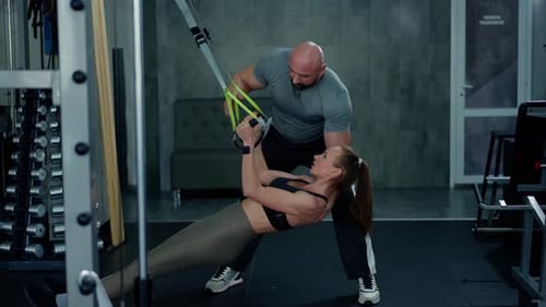 A Young Girl Athlete in the Gym Does Pull Ups on Sports Harness for Stretching A Man Fitness