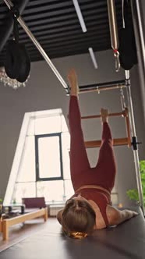 Woman Doing Pilates Exercises on Balanced Body Cadillac Machine at Studio Focusing on Strength and