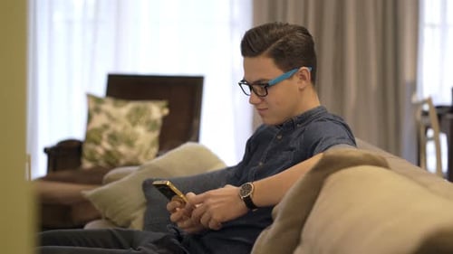 Teen Using Mobile Phone Relaxing on Couch at Home