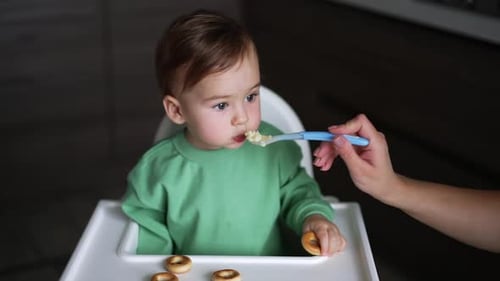 Infant Eating Food with Spoon in High Chair
