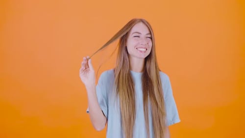 Smiling Woman Twirling Hair Strand on Orange Background