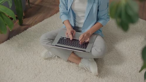 Lächelnde junge Frau sitzt an einem Laptop auf dem Boden zwischen Blumen