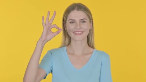 Woman Smiling Gives OK Gesture, Yellow Background